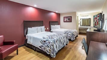 Habitación de hotel con dos camas, un escritorio, una silla, un televisor y un baño con espejo y lavamanos.