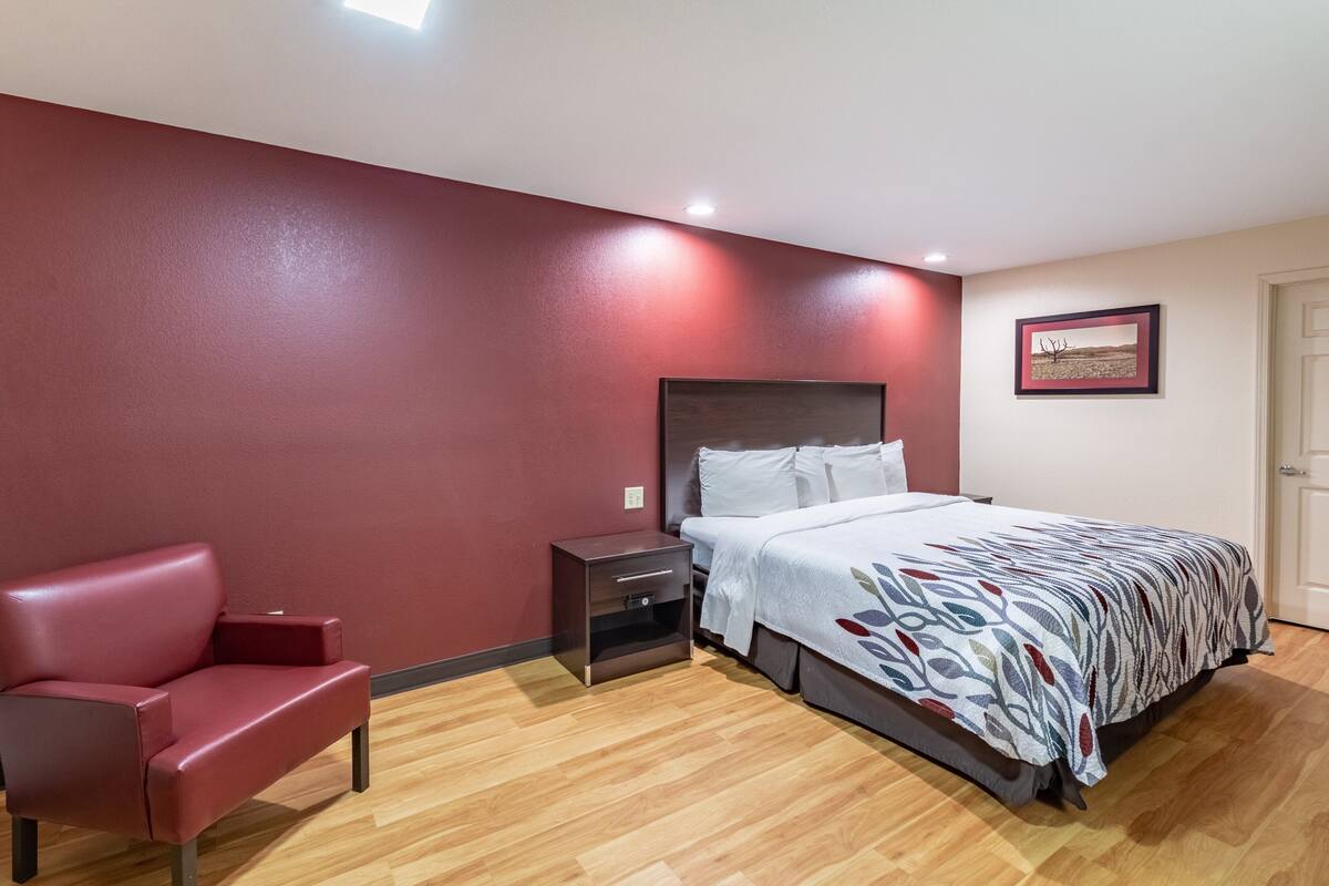 Ein Schlafzimmer mit roter Wand, einem Bett mit gemustertem Überwurf, einem roten Sessel und einem Nachttisch.