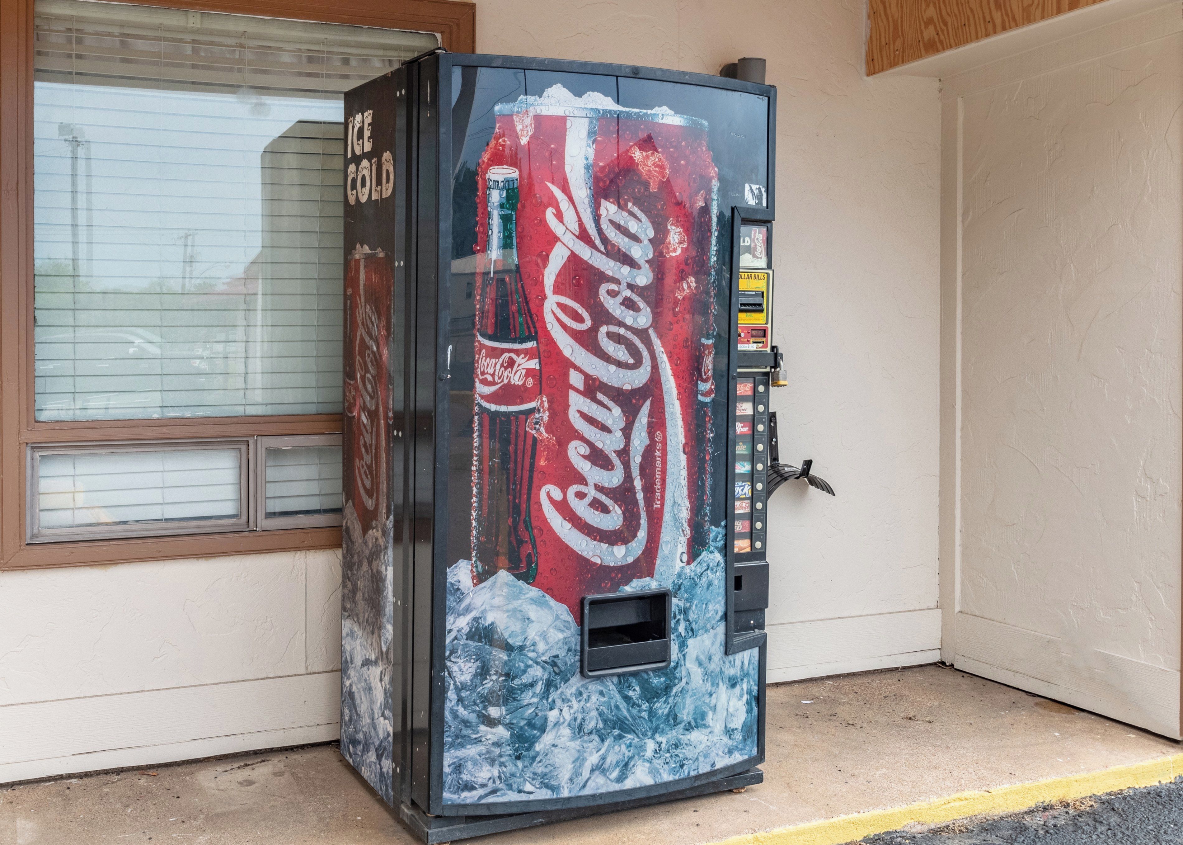 A Coca-Cola vending machine with a Coca-Cola logo, ice, and a yellow 'ILLAR BILLS' sign.