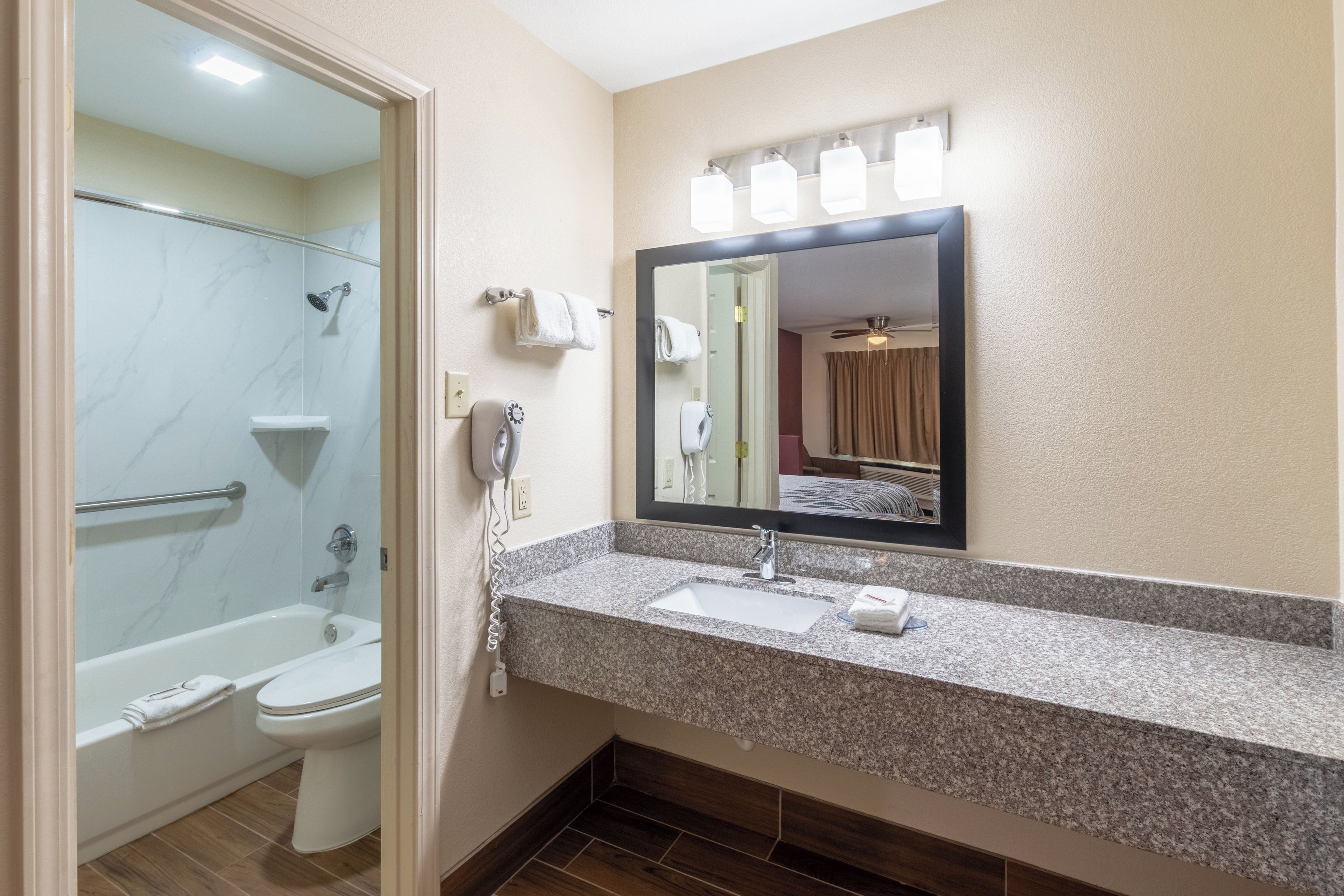 A bathroom with a shower, toilet, sink, and a mirror with lights above.