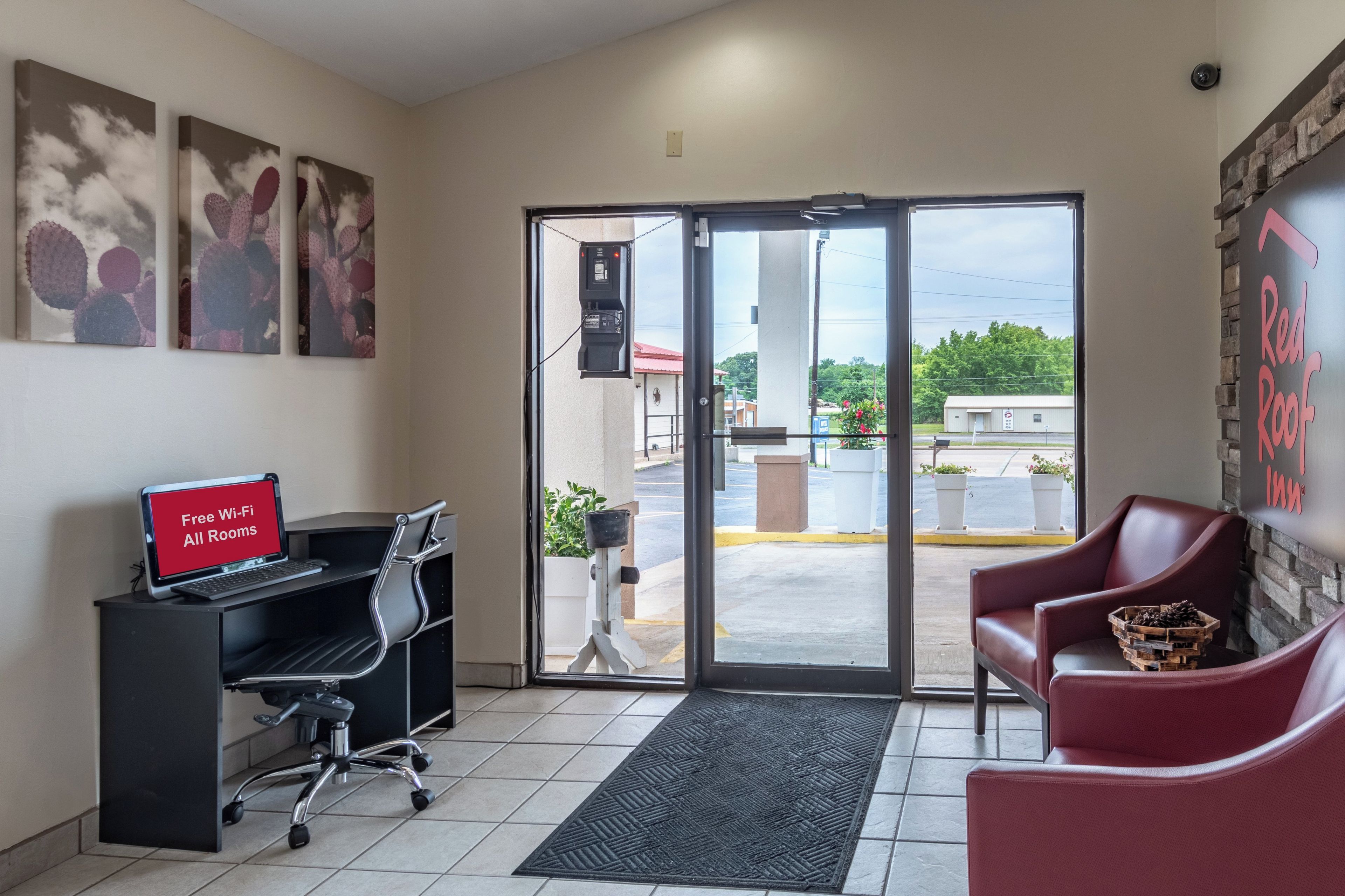 A hotel lobby with a desk, chairs, artwork on the walls, and a view through the glass doors.