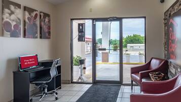 A hotel lobby with a desk, chairs, artwork on the walls, and a view through the glass doors.