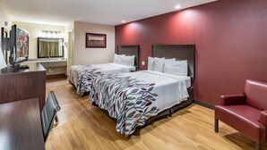 A hotel room with two beds, a desk, a TV, a mirror, and a red wall. - Red Roof Inn Buffalo, TX (Buffalo)