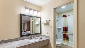 A bathroom with a granite countertop sink, a mirror, a toilet, and a shower with a striped curtain. - Red Roof Inn Buffalo, TX (Buffalo)