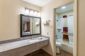 A bathroom with a granite countertop sink, a mirror, a toilet, and a shower with a striped curtain. - Red Roof Inn Buffalo, TX (Buffalo)