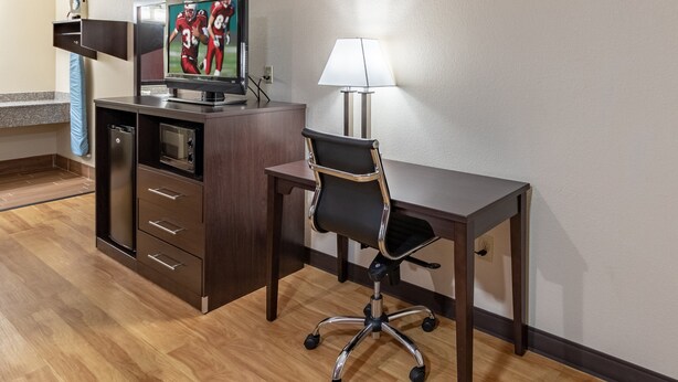 A hotel room with a wooden desk, a black office chair, a television on a cabinet, and a lamp on the desk. - Red Roof Inn Buffalo, TX (Buffalo)