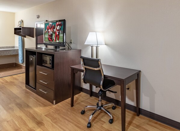 A hotel room with a wooden desk, a black office chair, a television on a cabinet, and a lamp on the desk. - Red Roof Inn Buffalo, TX (Buffalo)