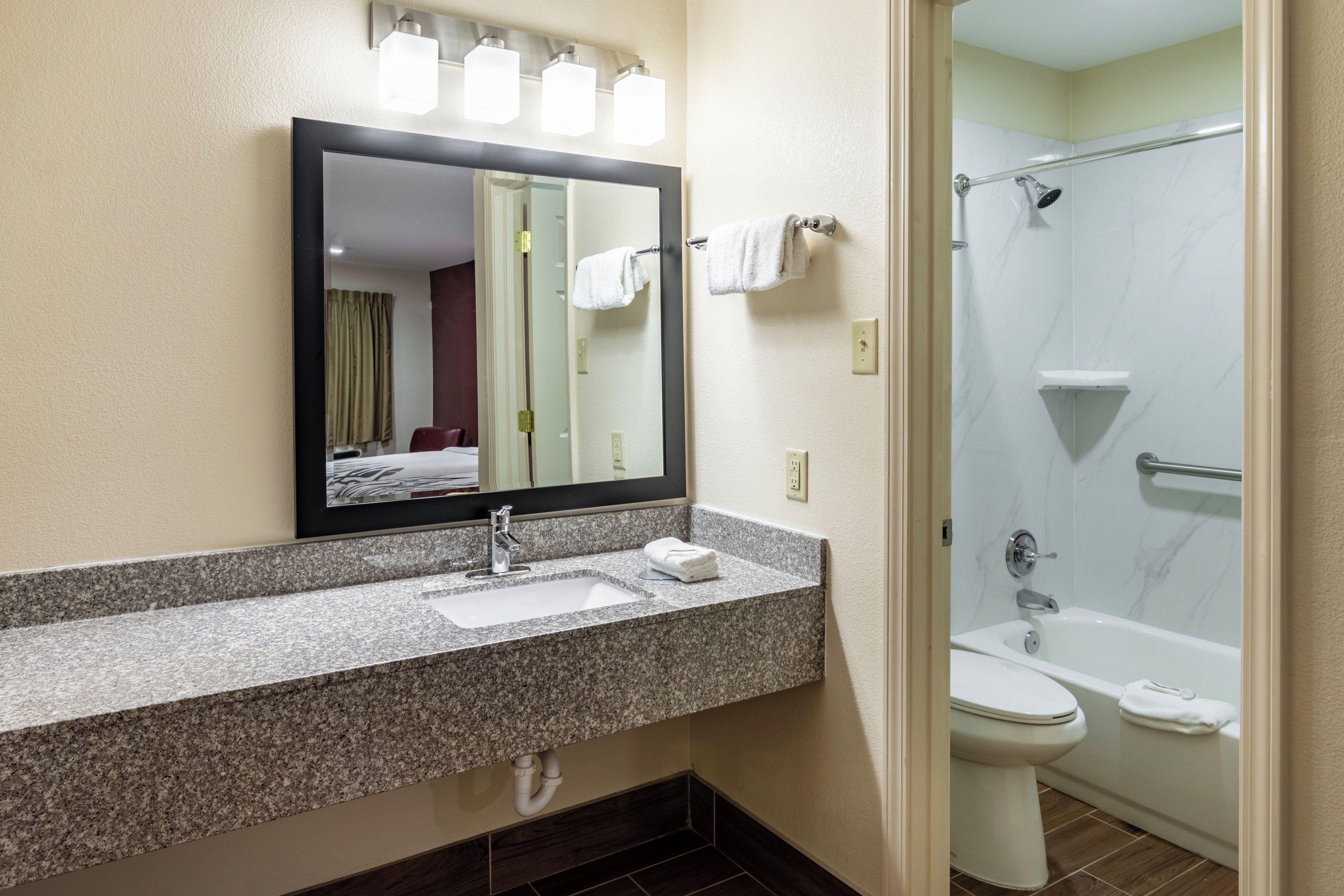 A hotel bathroom with a granite countertop, a sink, a mirror, a shower, and a toilet.