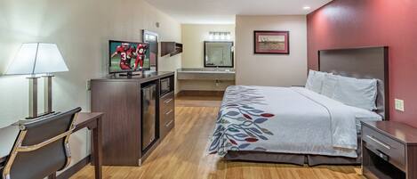 Una habitación de hotel con cama, escritorio con lámpara, televisión, espejo y baño.