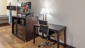 A hotel room with a desk, chair, television, and a small kitchenette.