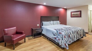 A hotel room with a bed, a red chair, a nightstand, and a framed picture on the wall. - Red Roof Inn Buffalo, TX (Buffalo)