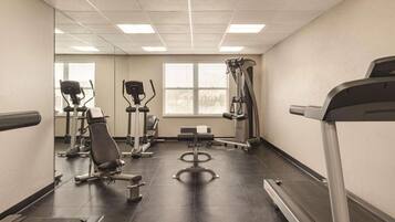 Un gimnasio con equipamiento de ejercicio, cinta de correr y una ventana con persianas.