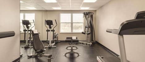 A gym with exercise equipment, a treadmill, and a window with blinds.
