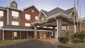 A multi-story building with a covered entrance, brick facade, and American flags. - Country Inn & Suites by Radisson, Boone, NC (Boone)