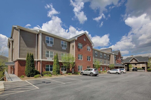 A multi-story hotel with a parking lot, several cars parked, and a clear sky.