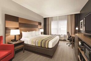 A hotel room with a large bed, two bedside tables with lamps, a red chair, a desk with a chair, and a television. - Country Inn & Suites by Radisson, Boone, NC (Boone)