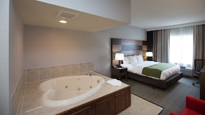 A hotel room with a large bathtub, a bed with a green throw, a nightstand with lamps, and a view of the outdoors through a window. - Country Inn & Suites by Radisson, Boone, NC (Boone)