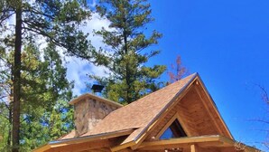 Eine Blockhütte mit einer Holztreppe, die zu einer Veranda führt, umgeben von Bäumen und einem Steinfundament.
