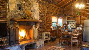 Ein rustikales Blockhaus-Interieur mit Kamin aus Stein, Holztisch und Küchenzeile.