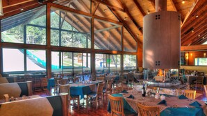 Ein geräumiges Restaurant mit hohen Decken und großen Fenstern, Holzmöbeln und einem zentralen Kamin.