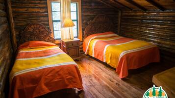 A cabin-style room with two wooden beds, a nightstand with a lamp, and a window with curtains.