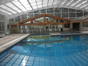 An indoor swimming pool with a glass ceiling, stone walls, and wooden beams. - Bosques De Monterreal (Arteaga)