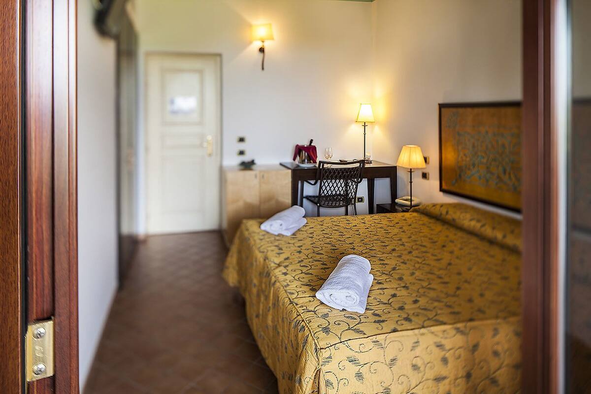 A hotel room with two beds, a desk, a chair, and a lamp.