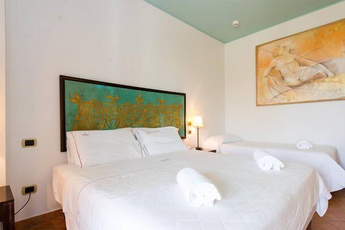 A hotel room with two beds, a painting on the wall, and a lamp.