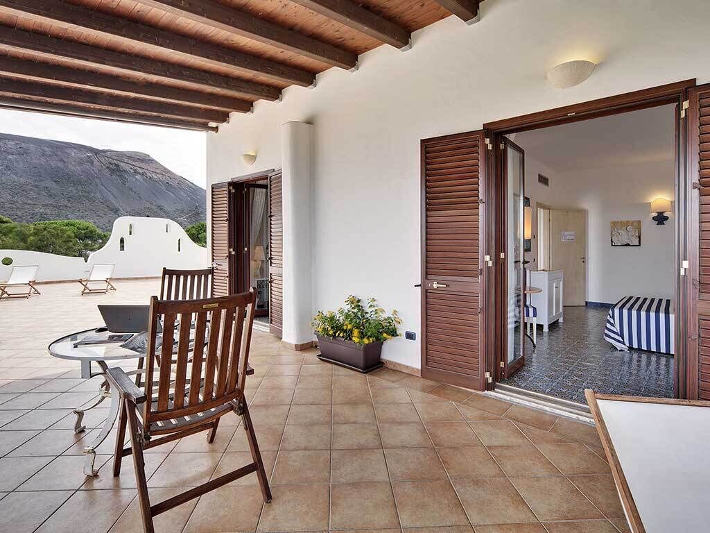 Uma área de estar coberta ao ar livre com uma cadeira de madeira, uma mesa e um vaso de planta.