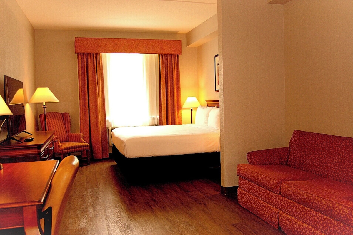 A hotel room with a bed, a desk with a lamp, a chair, and a sofa.