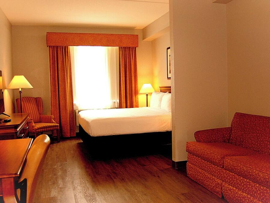 Una habitación de hotel con cama, escritorio con lámpara, silla y sofá.