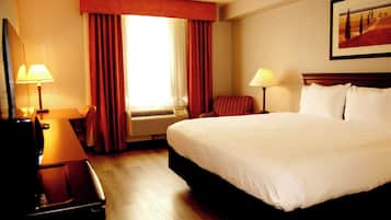 A hotel room with a large bed, two bedside tables with lamps, a window with curtains, and a painting on the wall.
