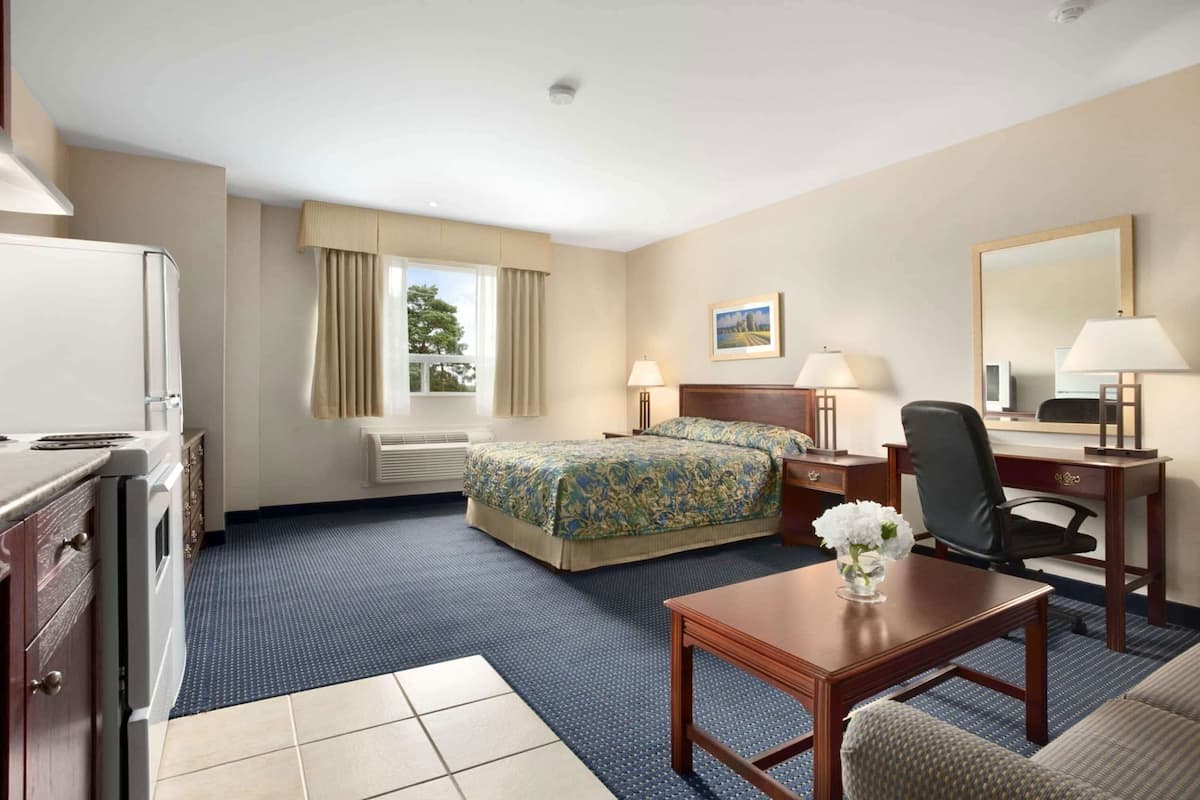 A hotel room with a bed, desk, chair, and a small table with a vase.