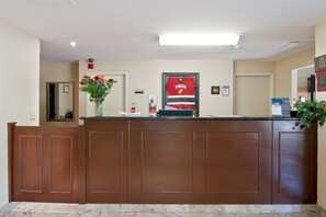 A reception desk with a framed sports jersey, a vase with flowers, and a fire extinguisher. - Travelodge by Wyndham Trenton (Quinte West)