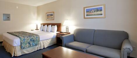 A hotel room with a bed, a sofa, a coffee table, and two bedside lamps.