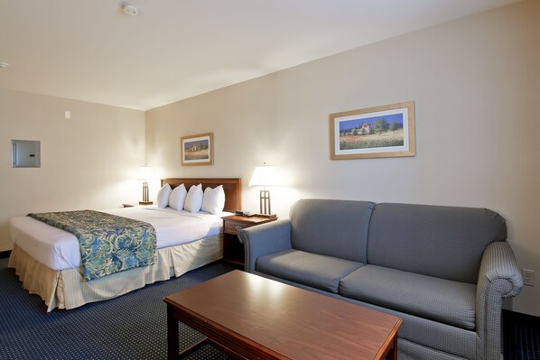 Una habitación de hotel con una cama, un sofá, una mesita de centro y dos lámparas de noche.