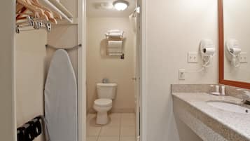 A bathroom with a sink, mirror, and hairdryer. There is a towel rack with towels and an ironing board.