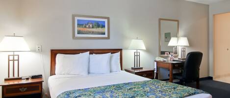 Habitación de hotel con una cama grande, dos mesitas de noche con lámparas, un escritorio con una silla y un cuadro en la pared.