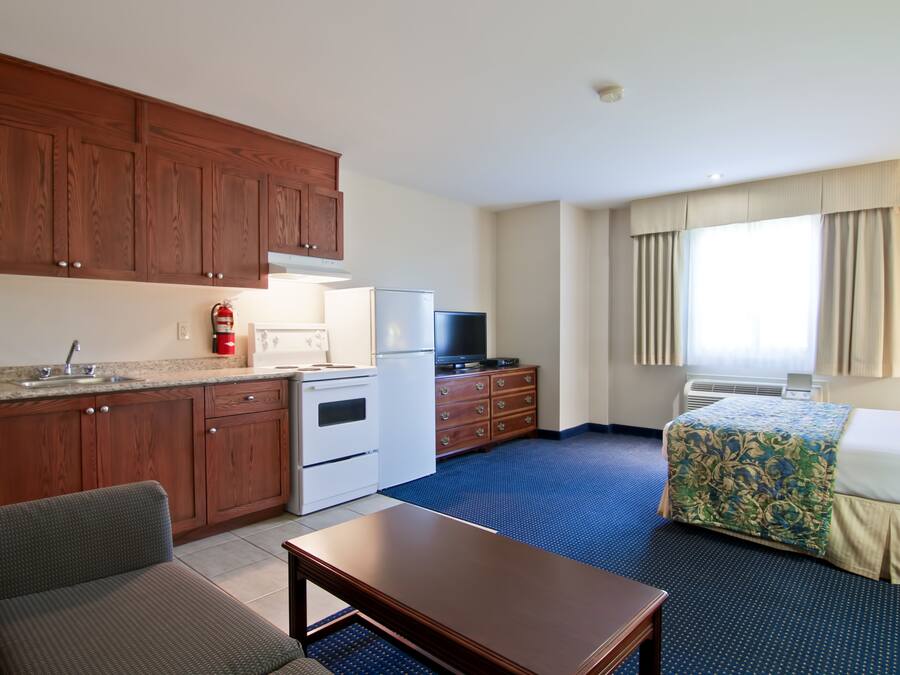 A hotel room with a kitchenette, a bed, a sofa, and a window with curtains.