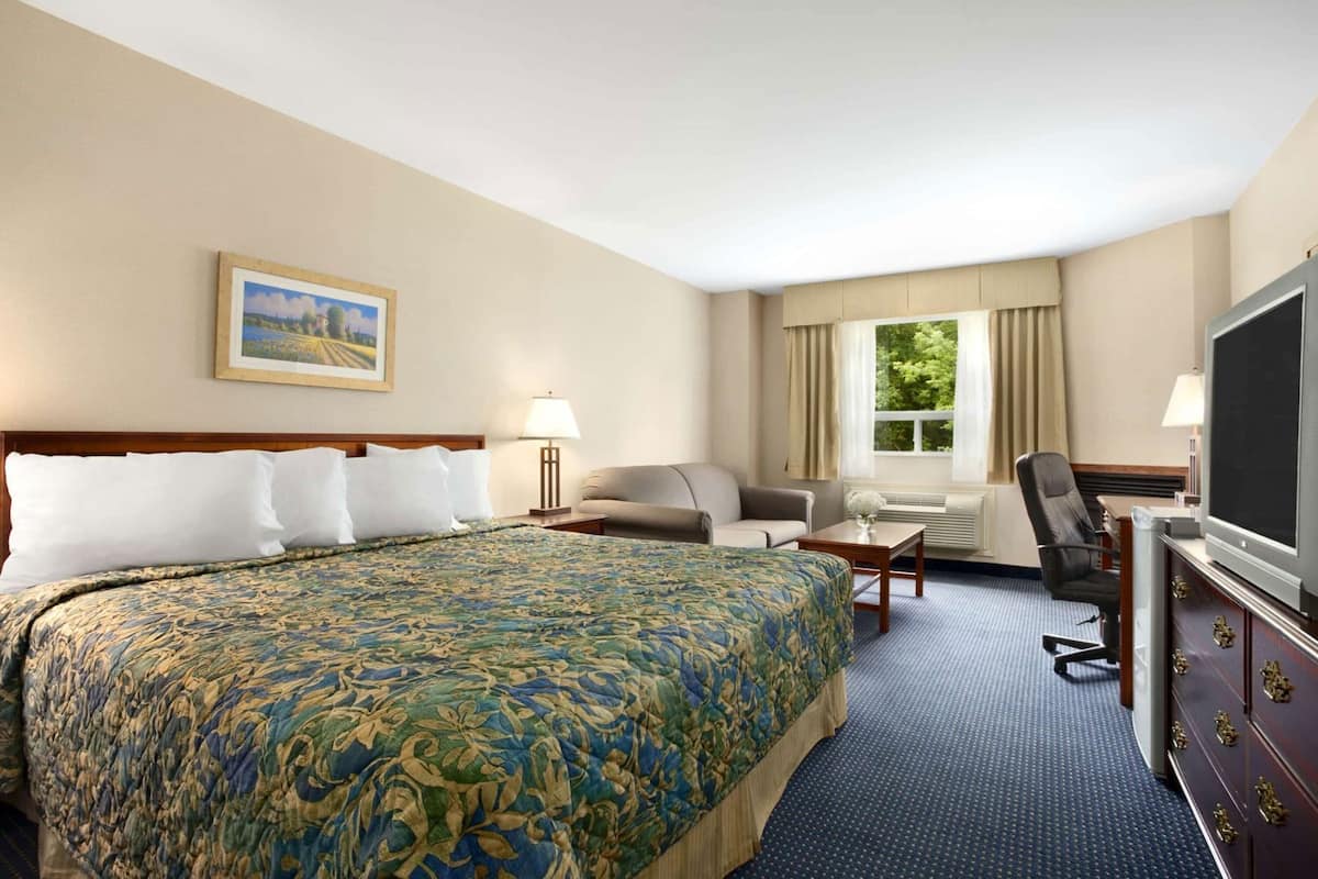 A hotel room with a large bed, a sofa, a desk, a TV, and a window with curtains.