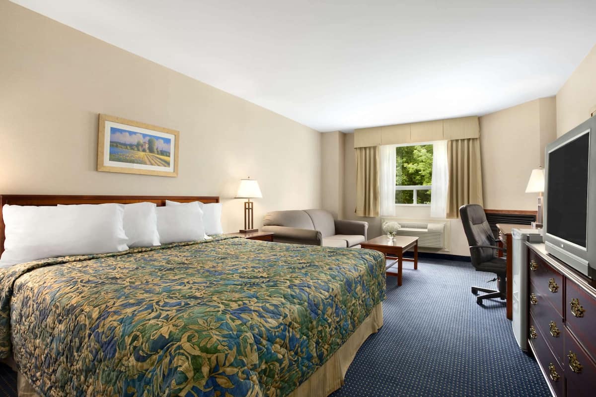 A hotel room with a large bed, a desk, a chair, a television, and a window with curtains.