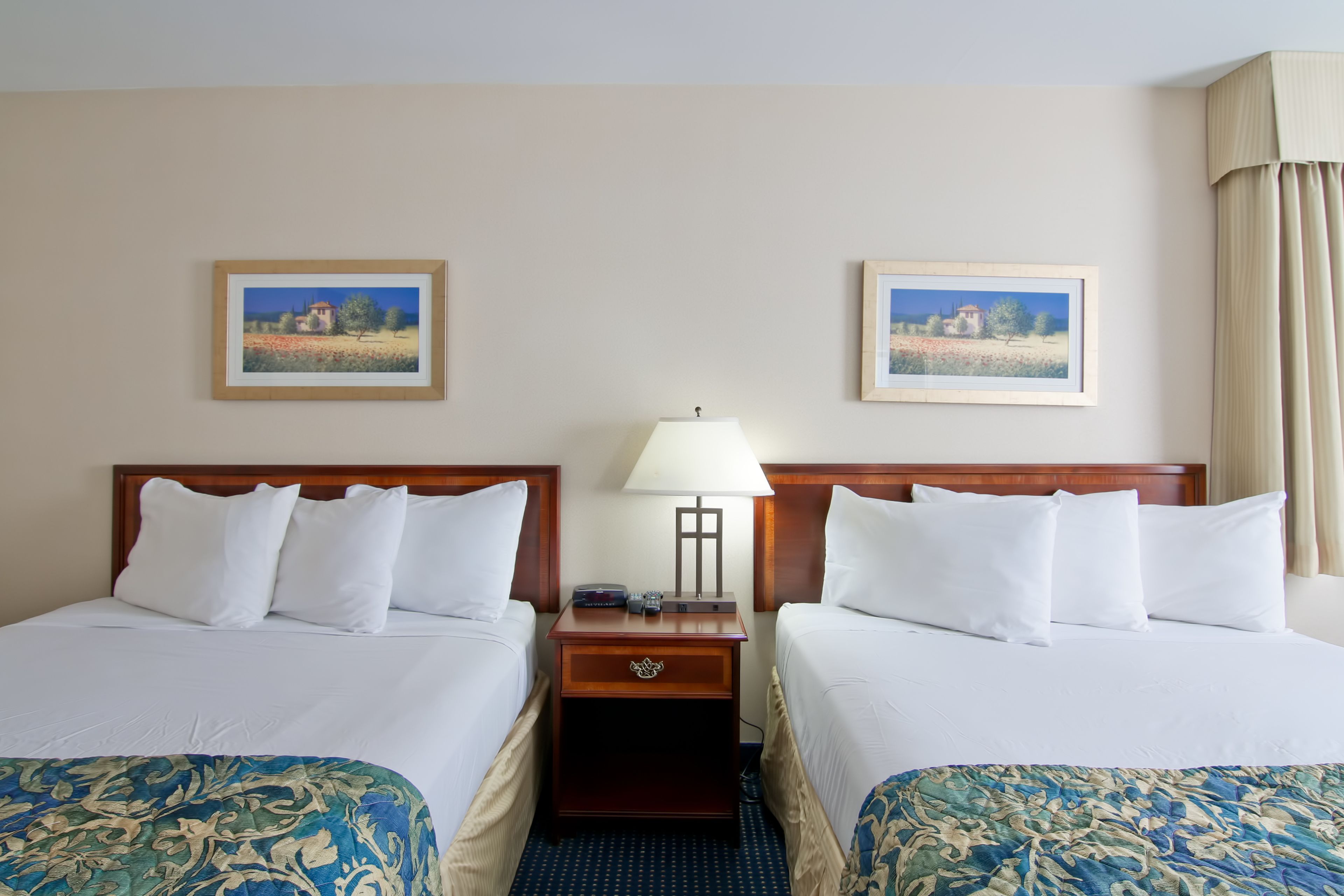 Une chambre d’hôtel avec deux lits, une table de chevet avec une lampe et deux tableaux encadrés au mur.