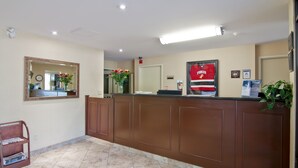 A reception area with a marble floor, wooden reception desk, a mirror, a vase with flowers, and a red banner. - Travelodge by Wyndham Trenton (Quinte West)
