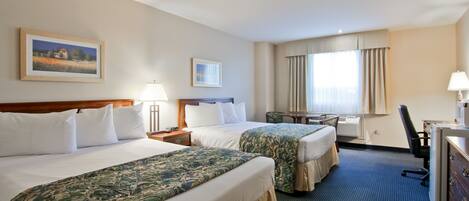 A hotel room with two beds, a desk, a chair, a lamp, and a painting on the wall.