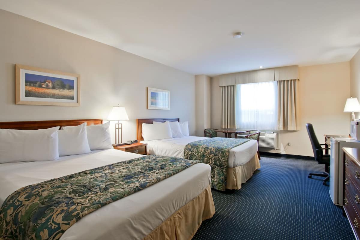 A hotel room with two beds, a desk, a chair, a lamp, and a window with curtains.
