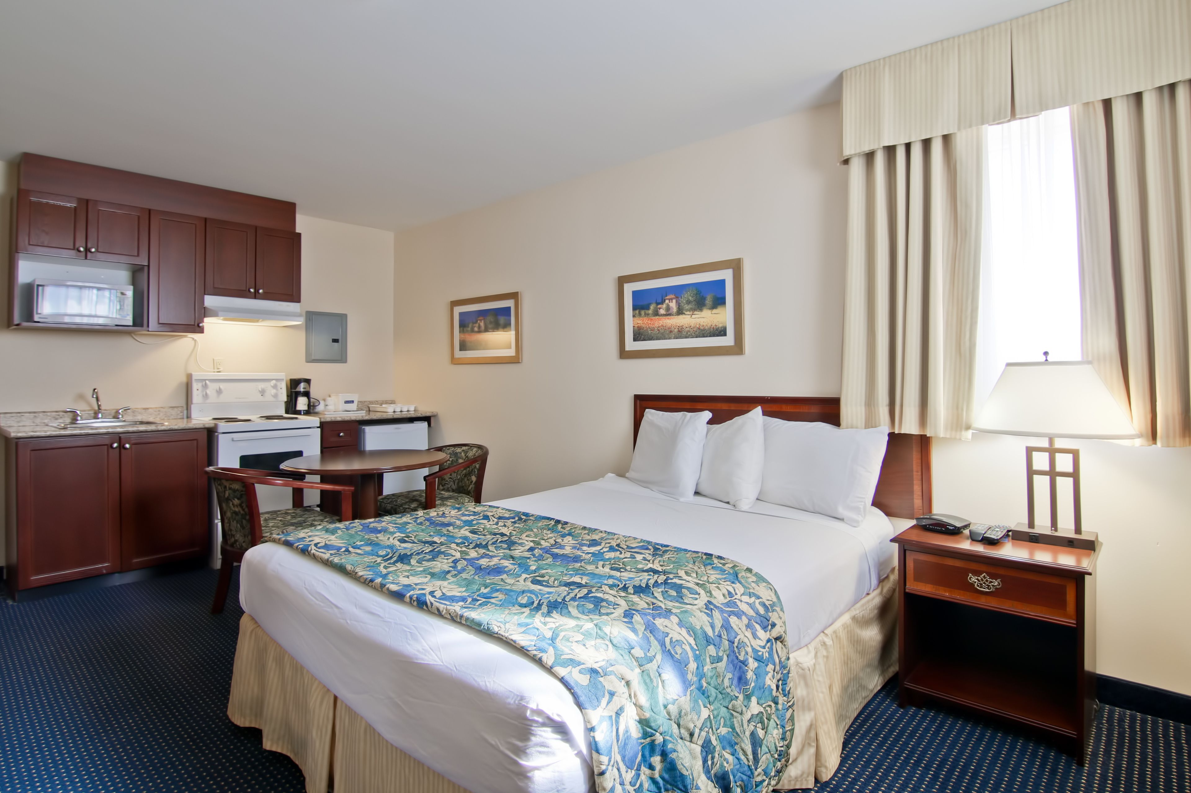 A hotel room with a bed, a desk, a microwave, a coffee maker, and a window with curtains.