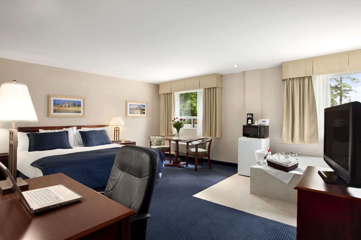 A hotel room with a bed, desk, chair, TV, and a small kitchenette.