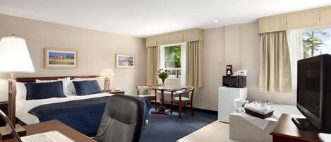 A hotel room with a bed, desk, chair, TV, and a small kitchenette.