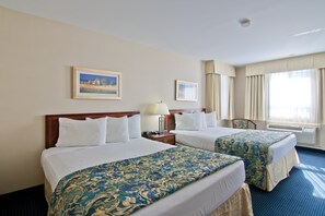 A hotel room with two beds, a nightstand, a lamp, a chair, and a window with curtains. - Travelodge by Wyndham Trenton (Quinte West)