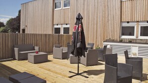 Une terrasse extérieure avec des meubles en osier, un parasol et une plateforme en bois.